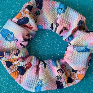 May include: A colorful scrunchie with a cartoon character print. The fabric features a tie-dye effect with pink, yellow, and blue hues. The characters are depicted in various poses, adding a playful touch to this hair accessory.