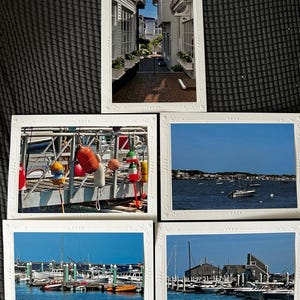 May include: Five white framed postcards featuring coastal scenes. One shows a brick alleyway between buildings. The others depict boats in a harbor, buoys, and a view of the water with boats and buildings under a blue sky.