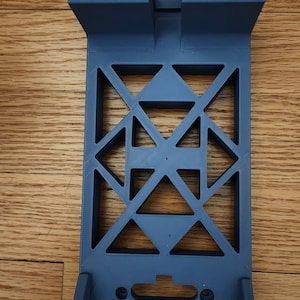 May include: A blue 3D printed phone stand with a geometric design. The stand has two slots for holding phones and a cutout for charging cables.