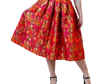 May include: A pink midi skirt with a floral pattern and gold accents. The skirt is pleated and has a high waist.