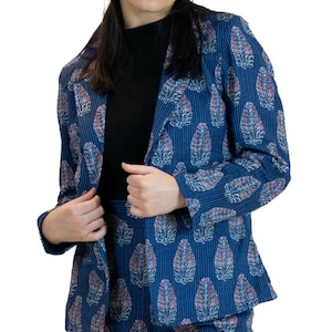 May include: A blue blazer and matching skirt set with a repeating leaf pattern in pink and white. The blazer is open, revealing a black top underneath. The fabric has a subtle striped texture. The outfit is a stylish ensemble.