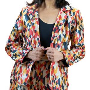 May include: A colorful blazer and matching pants set with a geometric pattern in red, yellow, navy, and cream. The blazer has a notched collar and long sleeves. The outfit is worn over a black top.