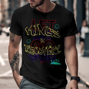 May include: Black t-shirt with a colorful graphic design that says "Let Kings Go In Recovery" with a smiley face and a small graphic of a hill with crosses.