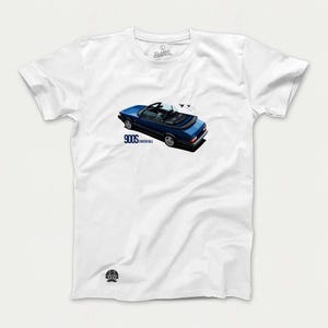 May include: White t-shirt with a blue Saab 900S convertible printed on the front. The car is driving down a road with a few airplanes flying overhead. The text "900S Convertible" is printed below the car.