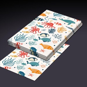 Op de afbeelding: Een stapel wit papier met een kleurrijk patroon van vissen, zeewier en zeesterren. Het patroon wordt op elk vel papier herhaald.