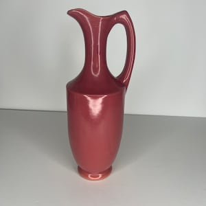 May include: A red ceramic pitcher with a wide mouth and a handle. The pitcher has a smooth, glossy finish.