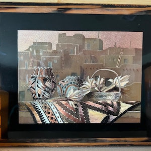 May include: A framed artwork depicting a Southwestern scene with adobe buildings, a woven rug, and three pottery vessels. The pottery is decorated with geometric patterns in shades of brown, blue, and white. The background features a sunset sky.