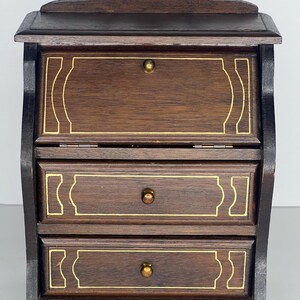 Puede incluir: Un escritorio de madera marr&oacute;n oscuro con tres cajones y una tapa abatible. Los cajones tienen ribetes dorados y pomos de lat&oacute;n. El escritorio tiene un frente curvo y una parte superior festoneada.