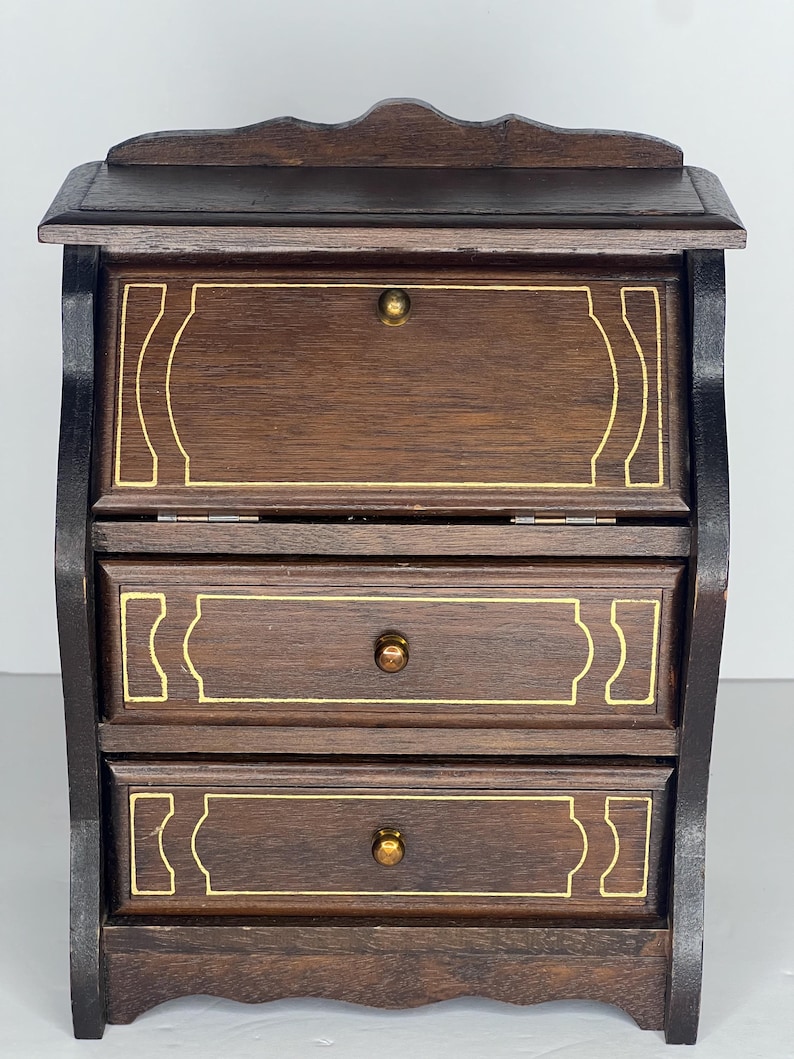 Puede incluir: Un escritorio de madera marr&oacute;n oscuro con tres cajones y una tapa abatible. Los cajones tienen ribetes dorados y pomos de lat&oacute;n. El escritorio tiene un frente curvo y una parte superior festoneada.
