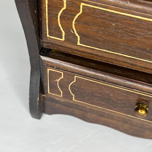 Puede incluir: Una caja de madera para joyas con dos cajones. Los cajones tienen ribetes dorados y un dise&ntilde;o decorativo. La caja tiene un acabado marr&oacute;n oscuro.
