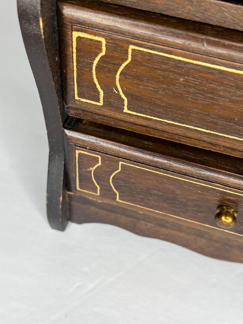 Puede incluir: Una caja de madera para joyas con dos cajones. Los cajones tienen ribetes dorados y un dise&ntilde;o decorativo. La caja tiene un acabado marr&oacute;n oscuro.