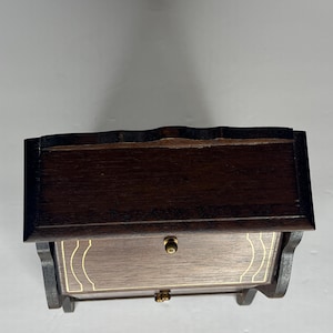 Puede incluir: Una caja de madera marr&oacute;n oscuro con un caj&oacute;n y una tapa con bisagras. La caja tiene un ribete dorado alrededor de los bordes del caj&oacute;n y la tapa.
