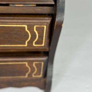 Puede incluir: Una caja de madera con tres cajones, cada uno con un dise&ntilde;o de borde dorado. La caja es de color marr&oacute;n oscuro y tiene un borde negro.