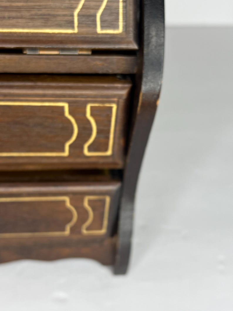 Puede incluir: Una caja de madera con tres cajones, cada uno con un dise&ntilde;o de borde dorado. La caja es de color marr&oacute;n oscuro y tiene un borde negro.