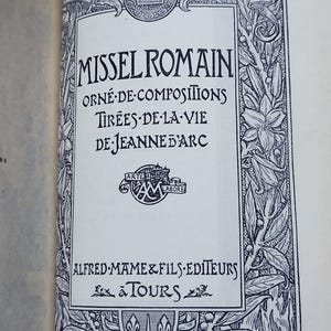 May include: A detailed book page with the title "MISSEL ROMAIN" in elaborate lettering. The page is framed by an intricate border of floral and foliate designs, with text in French. The publisher's name, Alfred Mame & Fils, is also visible.