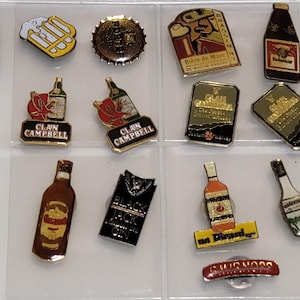 Puede incluir: Una colección de pines de esmalte vintage con marcas de cerveza y licores. Los pines muestran varias formas de botellas, logotipos y texto, incluyendo "Clan Campbell", "Alaska" y "Buckler". La paleta de colores incluye oro, rojo y negro.