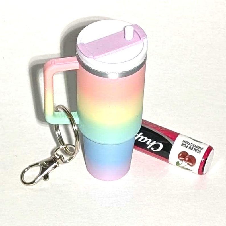 May include: A rainbow-colored travel mug with a lid and a straw, attached to a silver keychain. A cherry-flavored lip balm with the text "ChapStick Sealed for Protection" is also in the image.