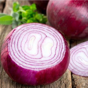 May include: A close-up of a sliced red onion, showcasing concentric rings of purple and white. The onion is on a wooden surface, with a few green herbs in the background. The vibrant colors and textures highlight the freshness of the produce.