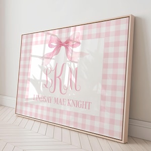 Puede incluir: Impresión en lienzo enmarcada con un borde de cuadros rosas. El centro blanco presenta un lazo rosa, las iniciales "KM" en cursiva y el nombre "LINDSAY MAE KNIGHT" debajo.
