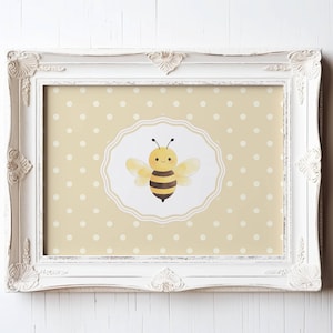May include: A framed print with a cartoon bee illustration. The bee is yellow and black, with a smiling face and wings. The background is a light yellow with white polka dots, and the frame is white with decorative detailing.