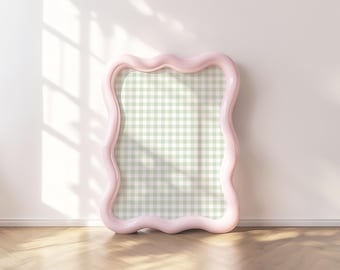 May include: A pink, wavy, decorative picture frame with a green and white gingham pattern inside. The frame is on a light wood floor.