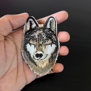May include: Embroidered wolf head patch with brown, black and white fur. The wolf has a white muzzle and a black nose.