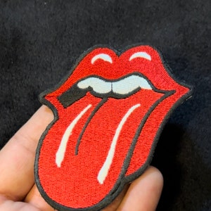 May include: Red and white embroidered patch of a tongue sticking out with a black outline. The tongue has two white lines down the middle.