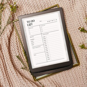 Könnte beinhalten: Ein schwarz-weißer druckbarer To-Do-Listen-Planer mit Abschnitten für das heutige Ziel, die Prioritätenliste, den Speiseplan, den heutigen Zeitplan und Notizen. Der Planer liegt auf einer rosa gestrickten Decke mit grünen Zweigen.