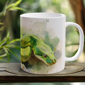 May include: White ceramic mug with a watercolor design of a green snake. The snake is curled up and has a light green and yellow pattern.
