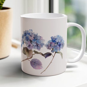 May include: White ceramic mug with a watercolor design of blue and purple hydrangeas on a white background.