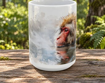 Puede incluir: Una taza de cerámica blanca con una ilustración estilo acuarela de un macaco japonés con cara roja y pelaje espeso. El mono está representado de perfil, mirando hacia la izquierda, con su reflejo visible en el agua debajo de él.