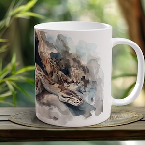 Puede incluir: Taza de cerámica blanca con una ilustración de acuarela de una serpiente marrón y blanca en un entorno de jungla.