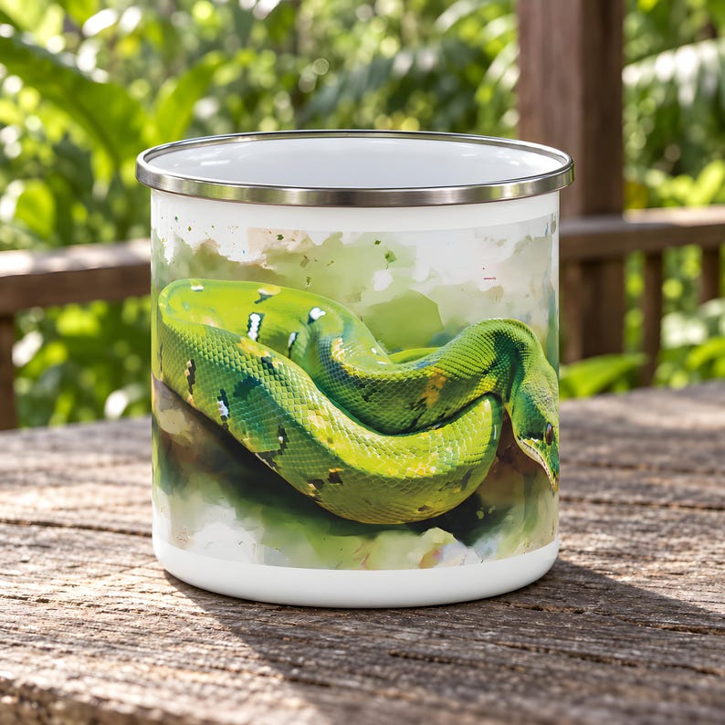 May include: A white enamel mug featuring a watercolor-style illustration of a vibrant green snake coiled on a branch. The mug has a smooth white interior and a polished silver-colored metal rim, providing a clean contrast to the detailed reptile art.
