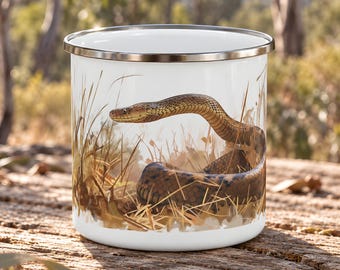 May include: A white enamel mug featuring a detailed illustration of a brown snake coiled within tall, dry grass. The mug has a smooth, cylindrical body and a metallic silver rim, showcasing a realistic depiction of the reptile in its natural habitat.