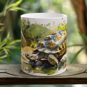May include: White ceramic mug featuring a watercolour illustration of a turtle in a pond. The turtle has a brown and yellow shell with black markings. The background is a green and brown watercolour wash.