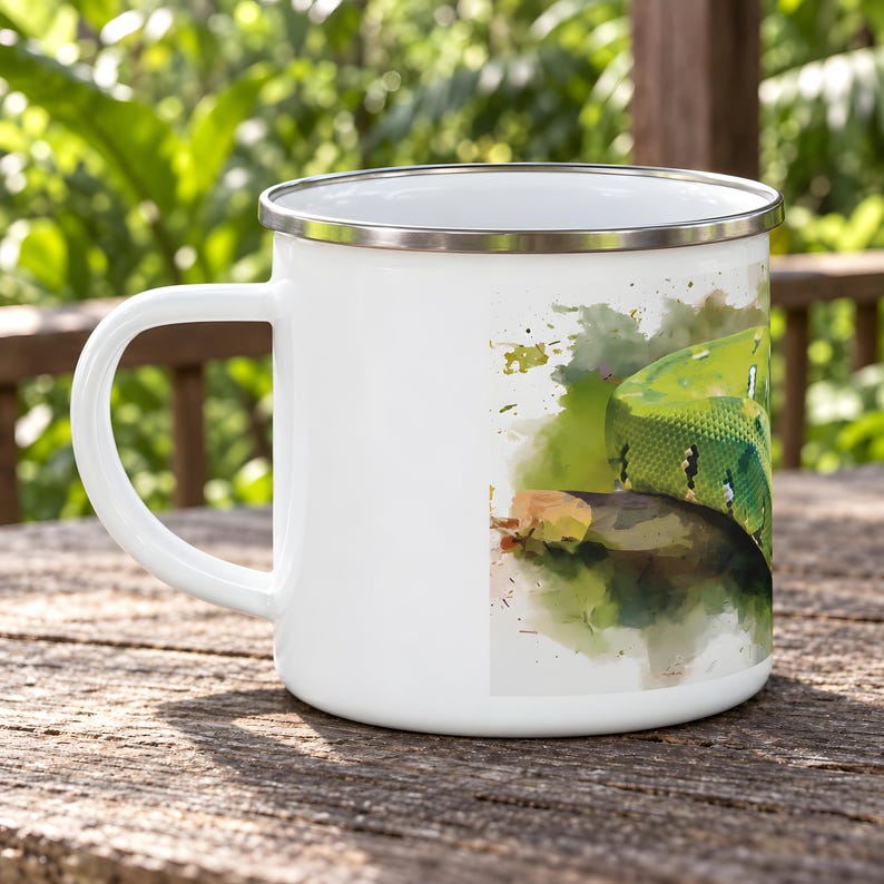 May include: A white enamel mug with a silver-toned rim and a handle on the left side. The mug features a watercolor-style illustration of a bright green snake coiled on a dark branch, set against a soft green and brown abstract background.