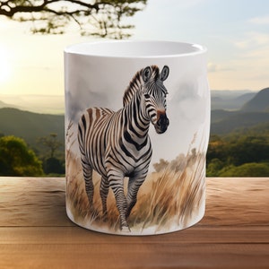 May include: White ceramic mug featuring a black and white zebra illustration. The zebra is standing in tall grass with a mountain range in the background.