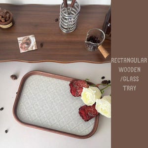 May include: A rectangular wooden tray with a glass surface and a brown wooden frame. The tray is decorated with red and white roses. The image also shows a wooden table with coffee beans and a small glass measuring cup.