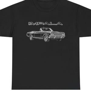以下が含まれることがあります： 黒の半袖Tシャツで、白い線画のクラシックなコンバーチブルカーのグラフィックが特徴です。車のイラストの上には、太字で白い縁取りのフォントで「IMPALA」という文字がプリントされており、車両が正面から側面にかけて描かれています。