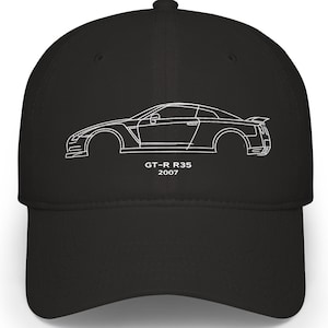 Puede incluir: Gorra de béisbol negra con un contorno blanco de un coche y el texto "GT-R R35 2007". La gorra tiene una visera curva y un ajuste estructurado. El diseño es una ilustración minimalista de un coche deportivo.
