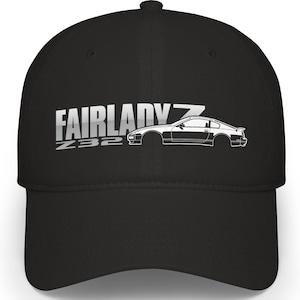 Puede incluir: Gorra de béisbol negra con el texto "FAIRLADY Z Z32" en plata y un contorno blanco de un coche deportivo. La gorra tiene una visera curva y una corona estructurada.