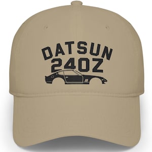 Puede incluir: Gorra de béisbol beige con el texto "DATSUN 240Z" en negro sobre una silueta de coche negro. La gorra tiene una visera curva y una corona estructurada.