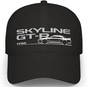 Puede incluir: Gorra de béisbol negra con el texto blanco "SKYLINE GT-R", una silueta de coche blanco y "R32". La gorra tiene una visera curva y una corona estructurada.