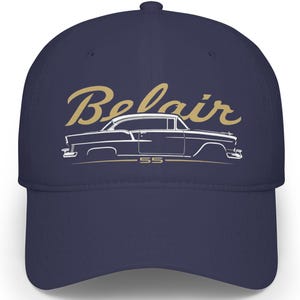 May include: A navy blue baseball cap featuring the word "Belair" in a gold script above a white outline of a classic car. The car's model year "55" is printed below the car. The cap has a curved brim and a structured fit.