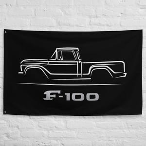 May include: Black wall flag featuring a white outline of a vintage F-100 pickup truck. The truck's design is detailed, with visible cab, bed, and wheels. The text "F-100" is displayed in silver below the truck.