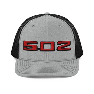 May include: A gray trucker hat with a black mesh back. The front of the hat features the red letters "502" in a bold, blocky font. The hat has a curved brim and a snapback closure.
