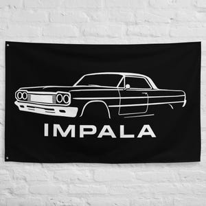 Op de afbeelding: Zwarte vlag met een witte omtrek van een klassieke Impala-auto. Het ontwerp van de auto omvat opvallende koplampen, een slanke carrosserie en het woord "IMPALA" in witte letters onderaan. De vlag hangt tegen een witte muur.