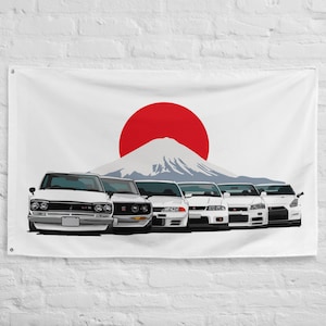 Puede incluir: Bandera blanca con un sol rojo y una silueta de montaña, con cinco coches deportivos blancos alineados. Los coches son de diferentes modelos. La bandera está colgada en una pared blanca.