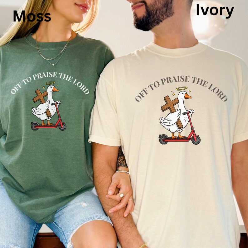 May include: Two t-shirts, one moss green and one ivory, each featuring a cartoon duck riding a red scooter and holding a cross. The text "OFF TO PRAISE THE LORD" arches above the duck. The duck has a halo.