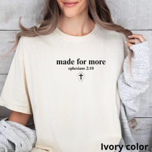 May include: Ivory-colored t-shirt with the text "made for more" above "ephesians 2:10" and a cross graphic. The shirt is a neutral color and has a simple, classic design.